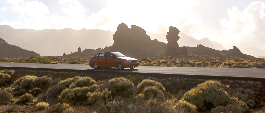 A car drives along a road through a desert rocky area at sunset